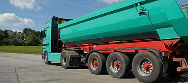 Lastkraftwagen mit Auflieger auf einer befestigten Fläche, im Hintergrund eine Landschaft.