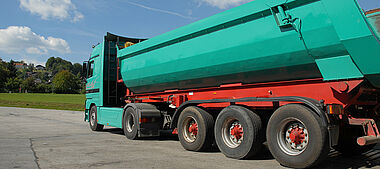Lastkraftwagen mit Auflieger auf einer befestigten Fläche, im Hintergrund eine Landschaft.