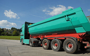 Lastkraftwagen mit Auflieger auf einer befestigten Fläche, im Hintergrund eine Landschaft.